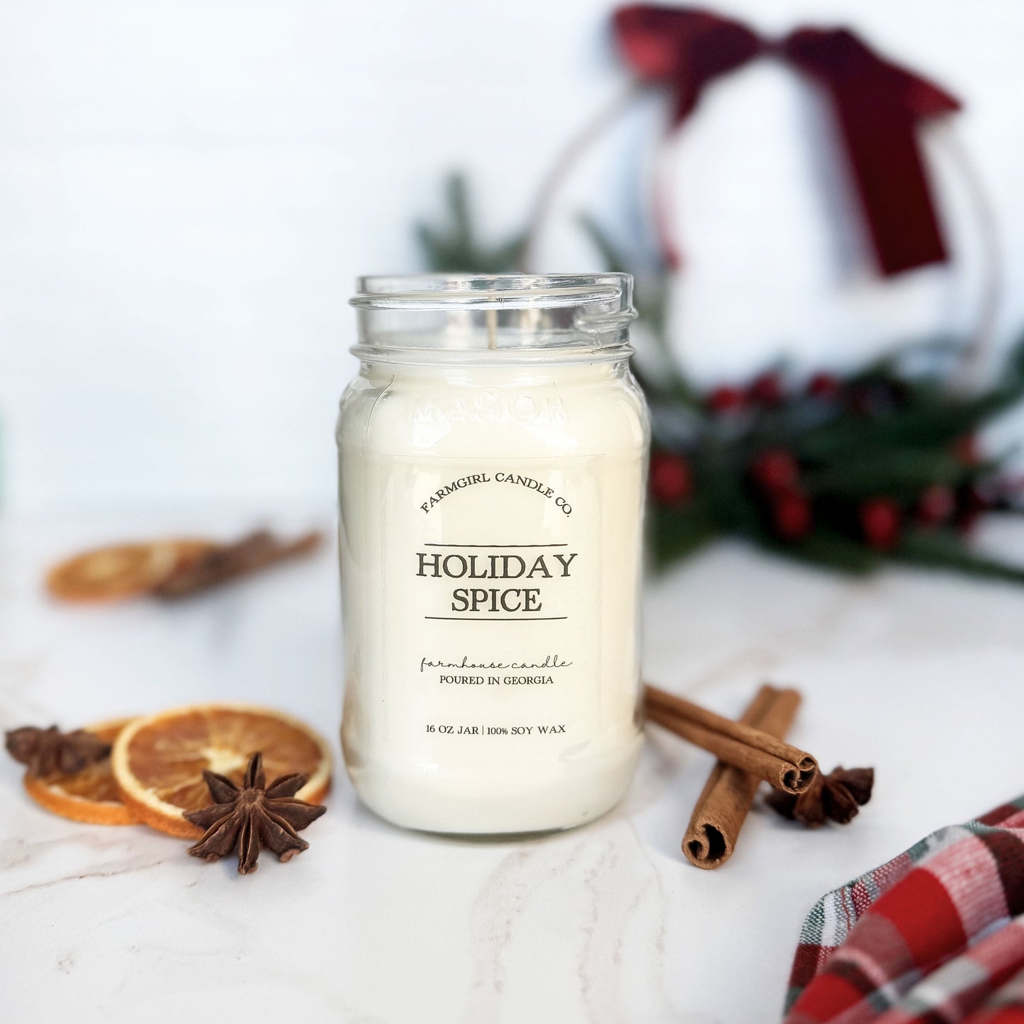 Candle labeled 'Holiday Spice' with cinnamon sticks and dried oranges on a white surface.