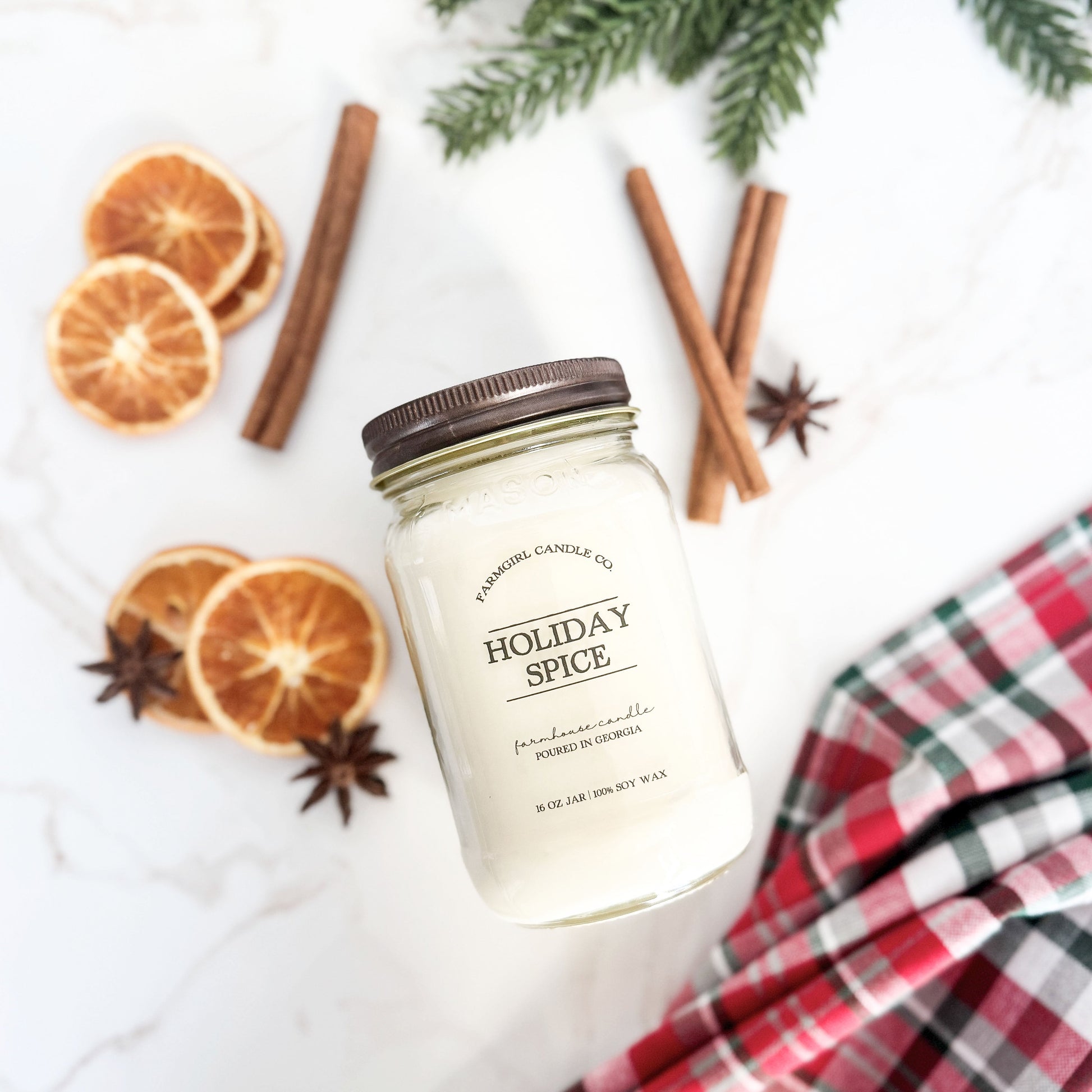 Mason Jar of 'Holiday Spice' candle with cinnamon sticks, oranges, and plaid fabric 